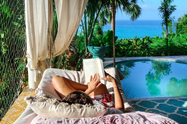 열대 식물과 수영장 근처 책을 읽고 의자 라운지에 누워있는 사람의 아름다운 샷