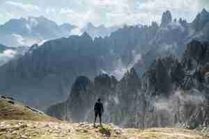 Free photo beautiful shot of person standing on a rock looking at three peaks nature park in toblach, italy