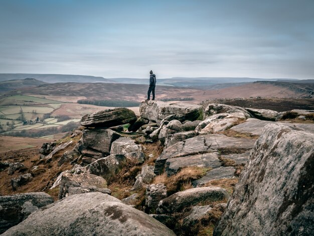 Красивый снимок человека, стоящего на скалах и смотрящего на долину вдалеке