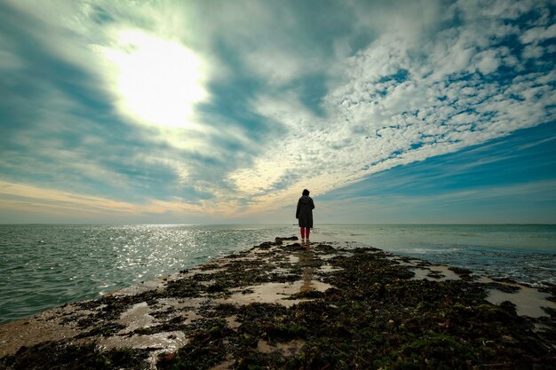 Beautiful shot of a person walking on a land inside the ocean under the cloudy sky