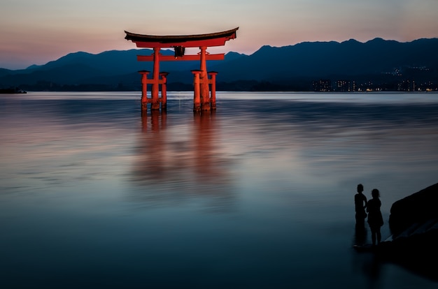 Beautiful shot of a red construction in the water with human silhouettes looking at it