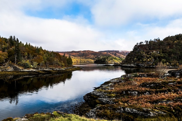 A beautiful shot of a river in the middle of forested mountains under a blue cloudy sky