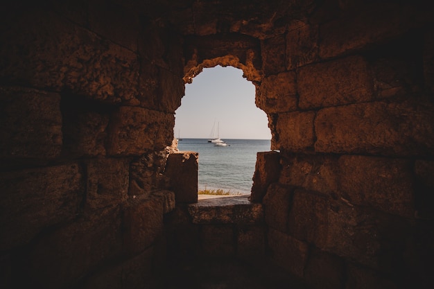 Beautiful shot of the sea with sailboats from the inside of a hole in a stone wall