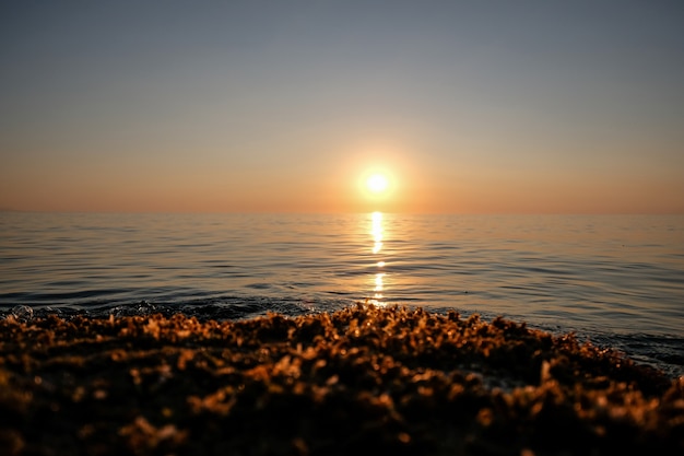 Красивый снимок моря с волнами и солнца на расстоянии с ясного неба на закате