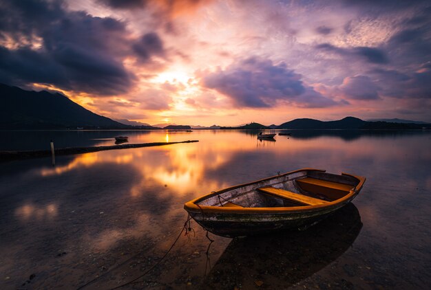 Beautiful shot of a small lake with a wooden rowboat in focus and amazing clouds in the sky