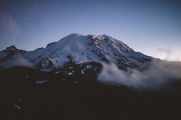 놀라운 별이 빛나는 하늘과 자연 안개로 둘러싸인 눈 덮인 산의 아름다운 샷