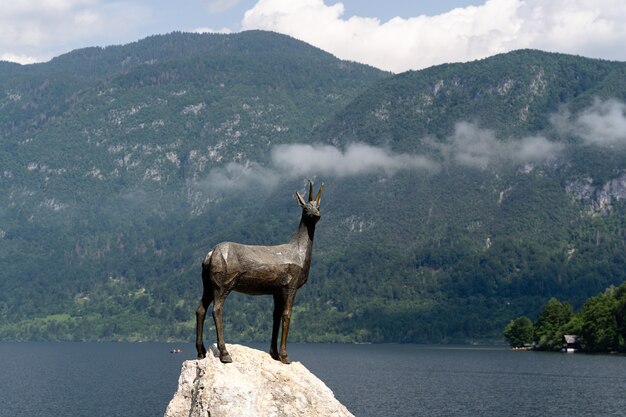 Beautiful shot of a statue to Goldhorn in Lake Bohinj surrounded by mountains and trees