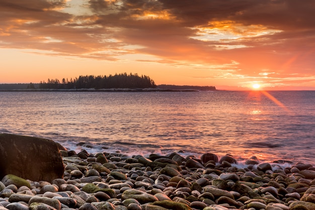 Красивый снимок каменистого берега моря и заходящего солнца на заднем плане