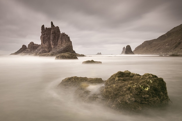 Beautiful shot of water flowing around large stones near the Benijo Rock on a cloudy day in Spain