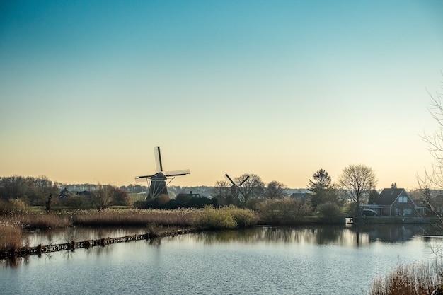 Beautiful shot of the windmill near the river surrounded by trees and houses