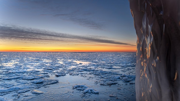 冬の風景、ひびの入った氷、雪、日没の海水のある海岸線の美しいショット。