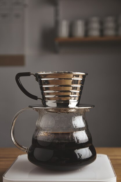 Beautiful side of transparent chrome drip coffee maker with roasted filtered coffee, isolated on thick wooden table in cafe shop. white weights. steam. brutal.