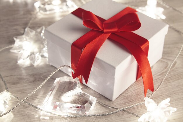 깜박이는 불빛으로 둘러싸인 빨간색 실크 테이프로 묶인 아름다운 간단한 빈 선물 상자. 세인트 발렌타인, 휴일, 축제, 생일을위한 낭만적 인 사랑스러운 선물