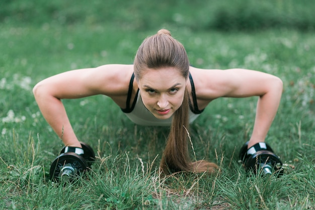 Beautiful slim brunette doing push ups workout on green grass in park