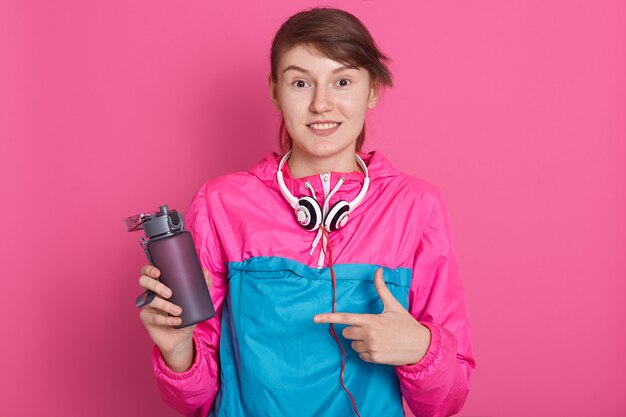 Beautiful slim brunette young girl wearing sports clothes posing. Sporty healthy model pointing to bottle of water