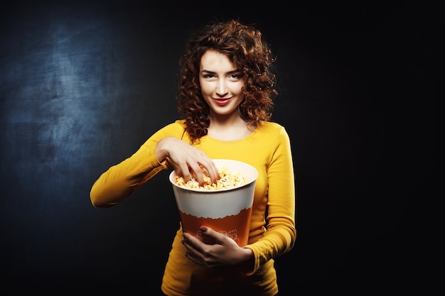 Красивая хитрая женщина хватает попкорн в ожидании интересного фильма