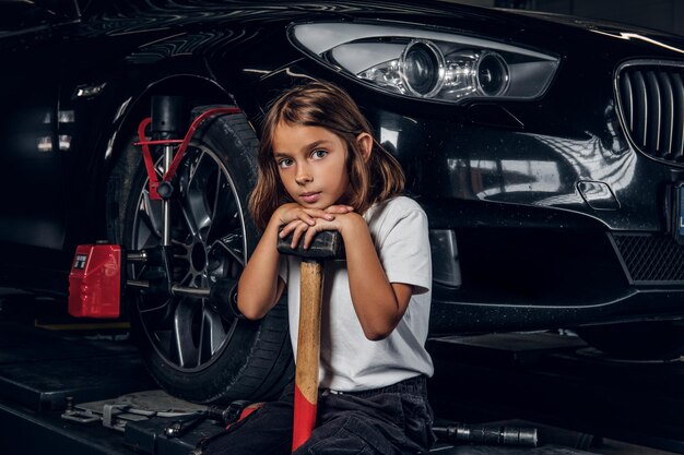 美しい小さな女の子が車とハンマーを持って高所作業車に座っています。