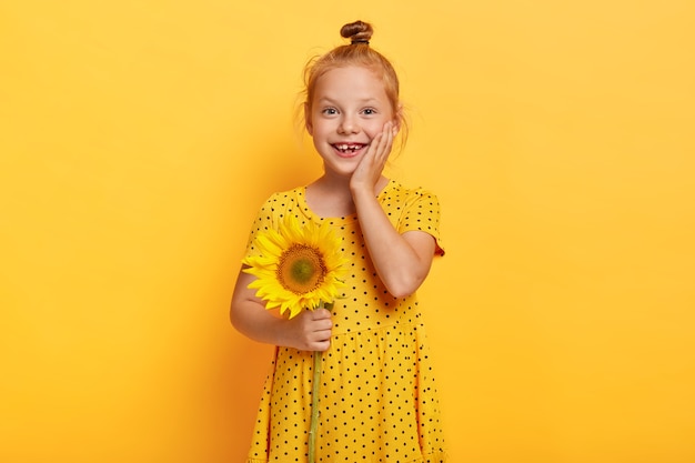 beautiful small red haired girl posing with sunflower in yellow dress