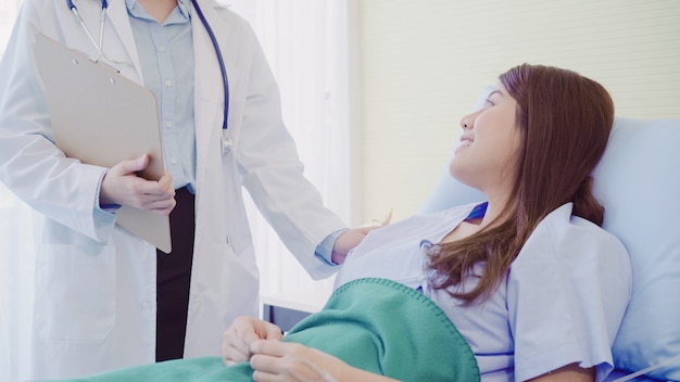 Beautiful smart Asian doctor and patient discussing and explaining something with clipboard