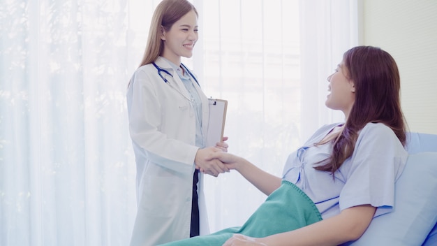 Beautiful smart Asian doctor and patient discussing and explaining something with clipboard 