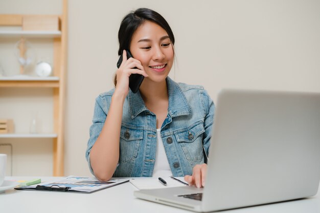 Free Photo beautiful smart business asian woman in smart casual wear working on laptop and talking on phone while sitting on table in creative office. 