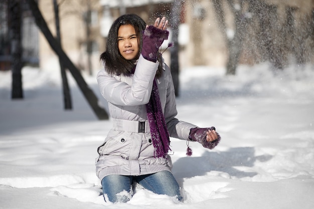 Free photo beautiful smiling american girl sitting in snow outdoors playing with snow