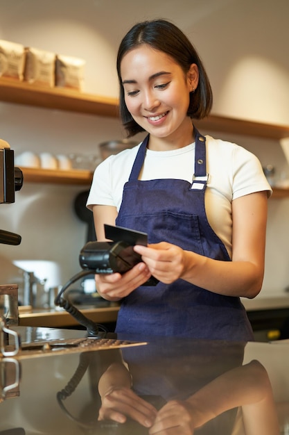 Free photo beautiful smiling asian girl barista insert client credit card in pos terminal processing payment ta