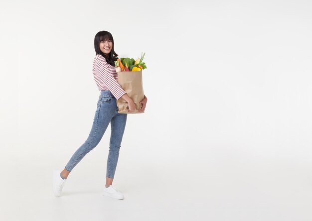 Красивая улыбающаяся азиатка держит сумку с продуктами и хочет скопировать пространство в сторону