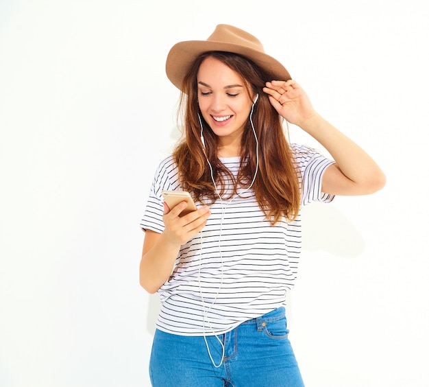 beautiful smiling brunette woman woman in casual hipster summer clothes with no makeup in brown hat listening music in phone with headphones
 isolated on white