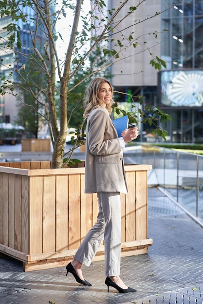 Beautiful smiling businesswoman drinks coffee on her working break standing on street