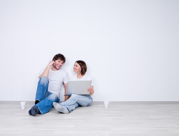 Beautiful smiling couple relax in the empty room with laptop