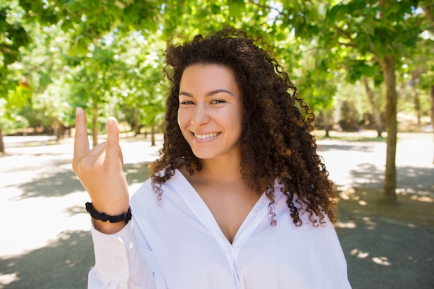 Free photo beautiful smiling curly woman showing devil horns sign