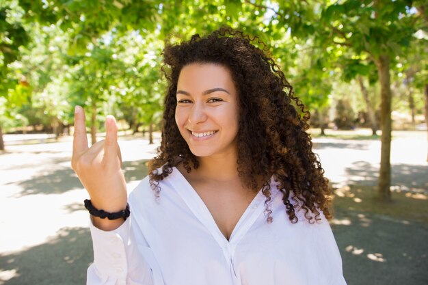 Beautiful smiling curly woman showing devil horns sign