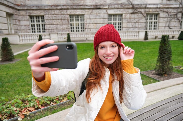 Free Photo beautiful smiling ginger girl in hat posing for photo on mobile phone takes selfie in park with cute