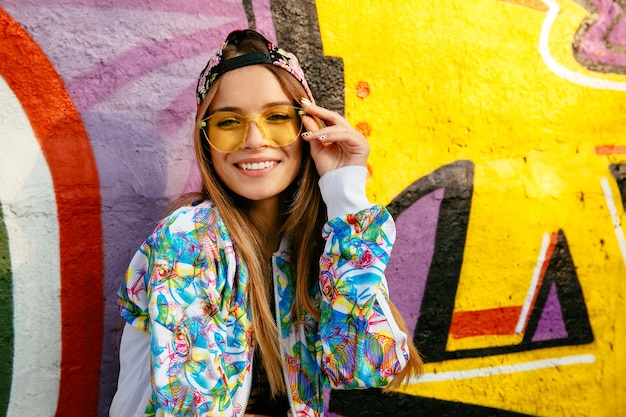 Beautiful smiling girl in eyeglasses, posing at camera. Dressed in stylish jacket and cap.
