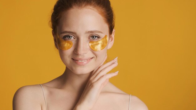 Beautiful smiling girl in gold eye patches confidently posing on camera over colorful background