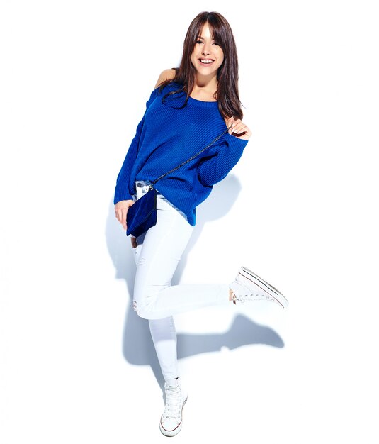 カジュアルなスタイリッシュな夏のセーターと白い背景に分離された青いハンドバッグの美しい笑顔ヒップスターブルネットの女性モデル。全長