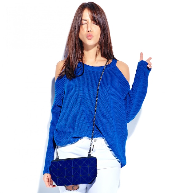캐주얼 세련 된 여름 스웨터와 파란색 핸드백에 아름 다운 미소 hipster 갈색 머리 여자 모델 평화 기호를 표시하고 키스를주는 흰색 배경에 고립