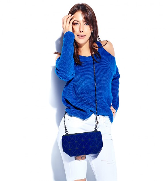 カジュアルなスタイリッシュな夏のセーターと白い背景で隔離された青いハンドバッグの美しい笑顔ヒップスターブルネットの女性モデル