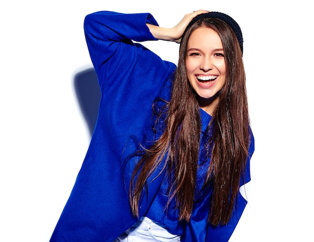 白で隔離されるスタイリッシュな青いオーバーコートで美しい笑顔ヒップスターブルネットの女性モデル