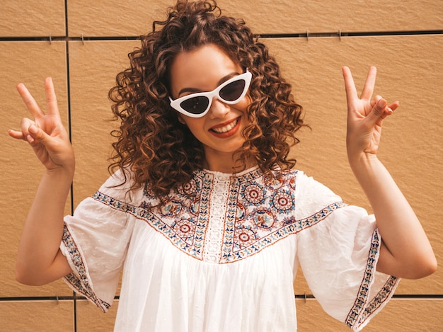 Foto gratuita il bello modello sorridente con l'acconciatura dei riccioli di afro si è vestito in vestito bianco ed occhiali da sole dai pantaloni a vita bassa dell'estate