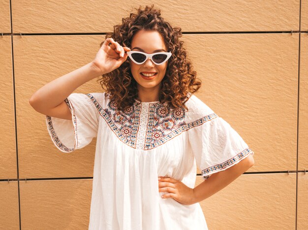 Beautiful smiling model with afro curls hairstyle dressed in summer hipster white dress and sunglasses