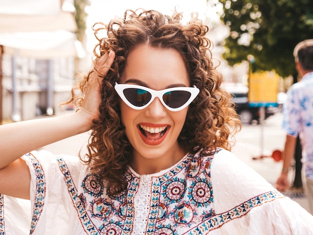 Beautiful smiling model with afro curls hairstyle dressed in summer hipster white dress.