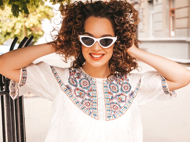 Beautiful smiling model with afro curls hairstyle dressed in summer hipster white dress