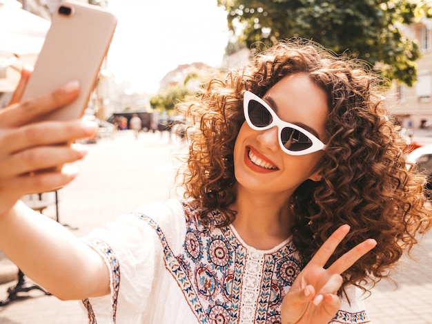 Beautiful smiling model with afro curls hairstyle dressed in summer hipster white dress.