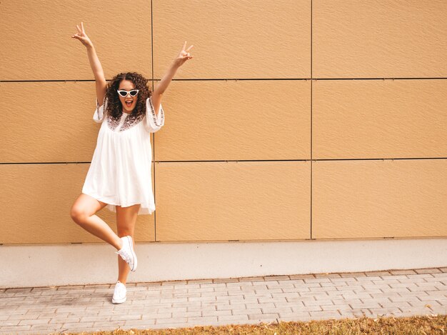 Beautiful smiling model with afro curls hairstyle dressed in summer hipster white dress.