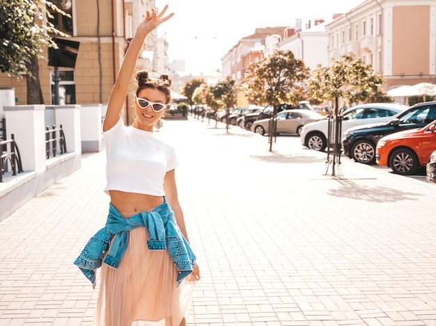 Beautiful smiling model with horns hairstyle dressed in summer hipster jacket jeans clothes.Sexy carefree girl posing in the street.Trendy funny and positive woman having fun in sunglasses