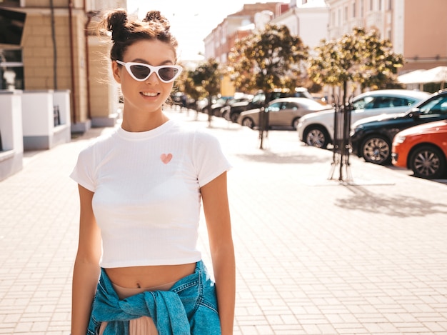 Beautiful smiling model with horns hairstyle dressed in summer hipster jacket jeans clothes.Sexy carefree girl posing in the street.Trendy funny and positive woman having fun in sunglasses