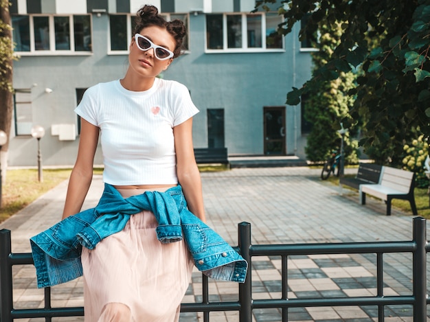 Beautiful smiling model with horns hairstyle dressed in summer hipster jacket jeans clothes.Sexy carefree girl posing in the street.Trendy funny and positive woman having fun in sunglasses