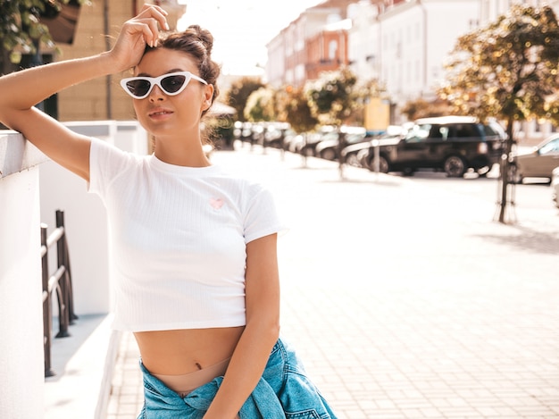 Beautiful smiling model with horns hairstyle dressed in summer hipster jacket jeans clothes.Sexy carefree girl posing in the street.Trendy funny and positive woman having fun in sunglasses